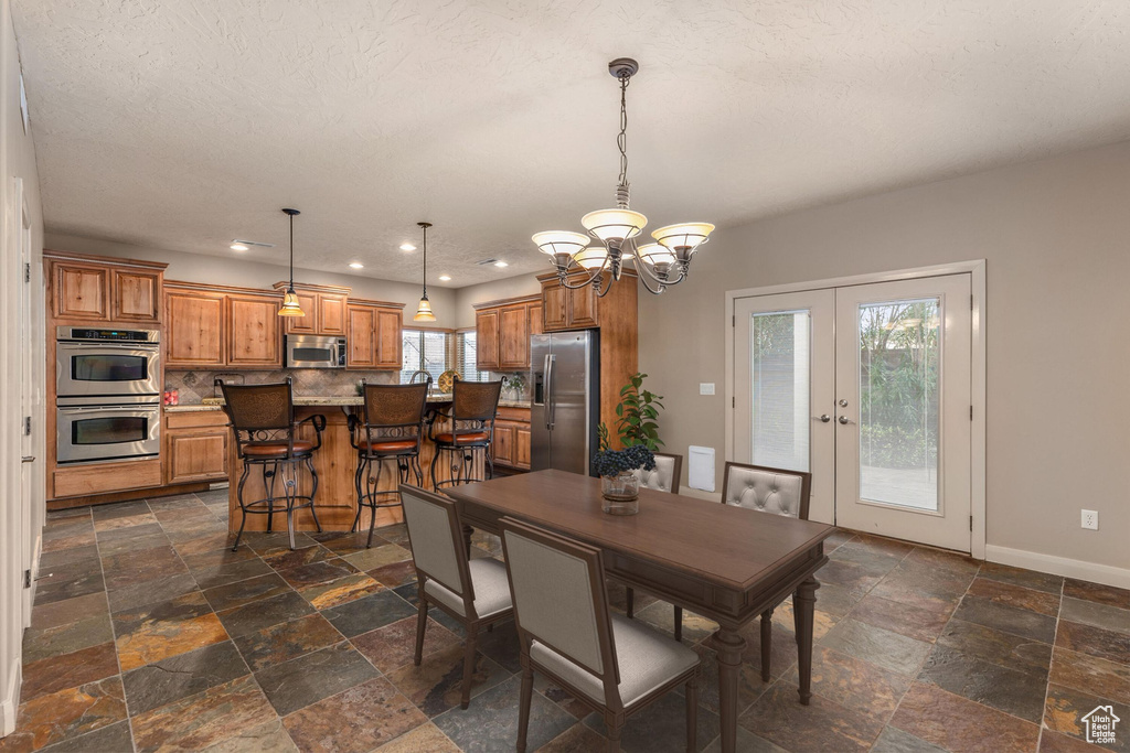 Dining space with an inviting chandelier, french doors, baseboards, and stone tile flooring