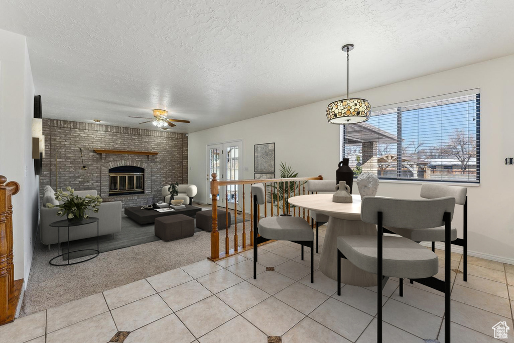 Dining space with a ceiling fan, a textured ceiling, light colored carpet, a brick fireplace, and light tile patterned floors
