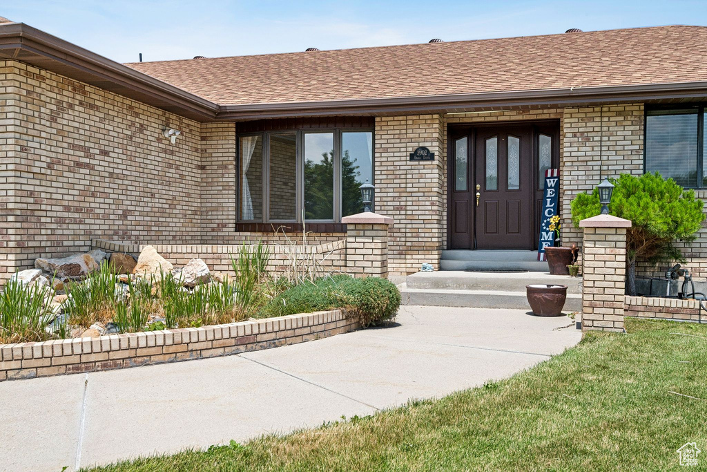 Doorway to property with brick siding and a shingled roof