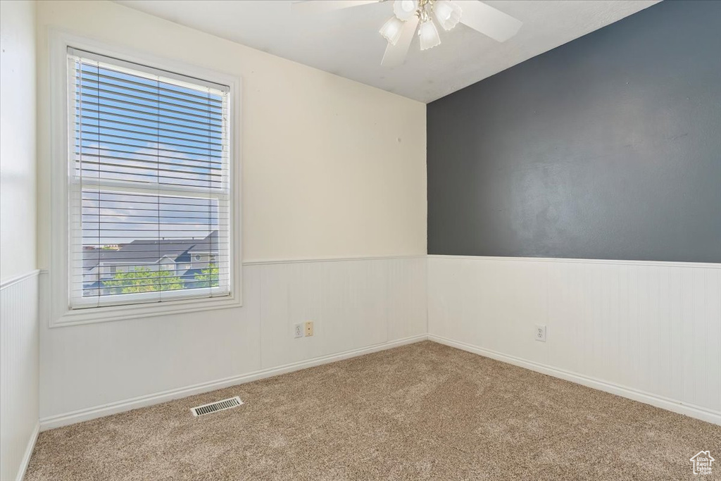 Unfurnished room featuring carpet flooring, wainscoting, and a ceiling fan