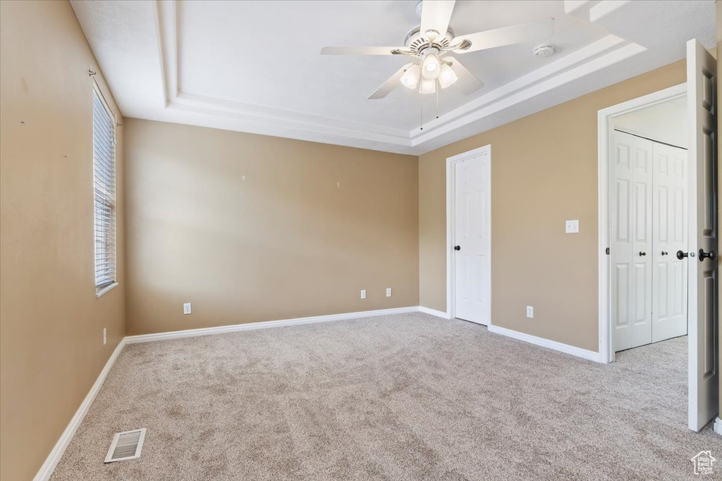 Unfurnished bedroom with a tray ceiling, carpet, baseboards, and a ceiling fan