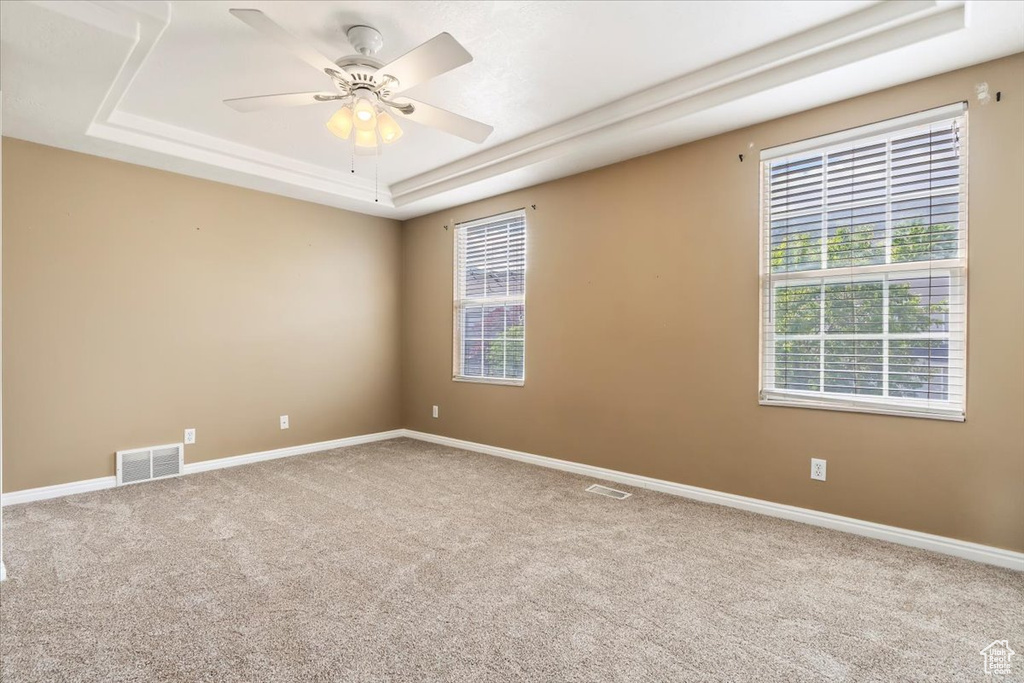 Spare room with a tray ceiling, carpet flooring, ceiling fan, and baseboards