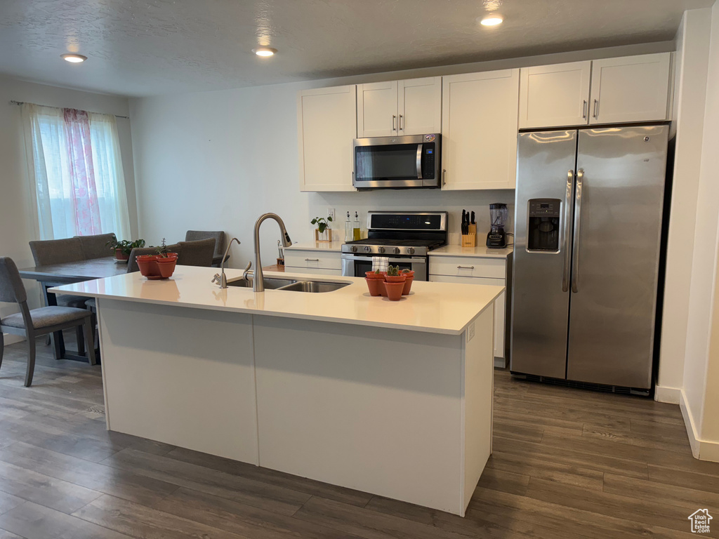 Kitchen with dark wood-type flooring, a sink, stainless steel appliances, white cabinets, and light countertops