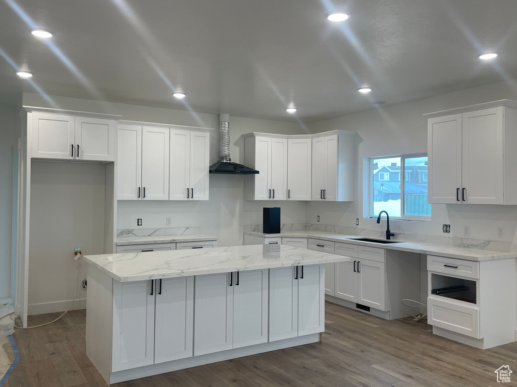 Kitchen with a kitchen island, wall chimney range hood, wood finished floors, white cabinets, and a sink