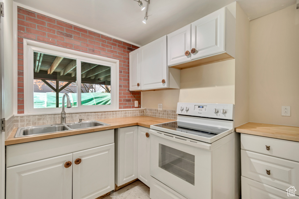 Kitchen featuring a sink, white cabinetry, white range with electric stovetop, brick wall, and rail lighting