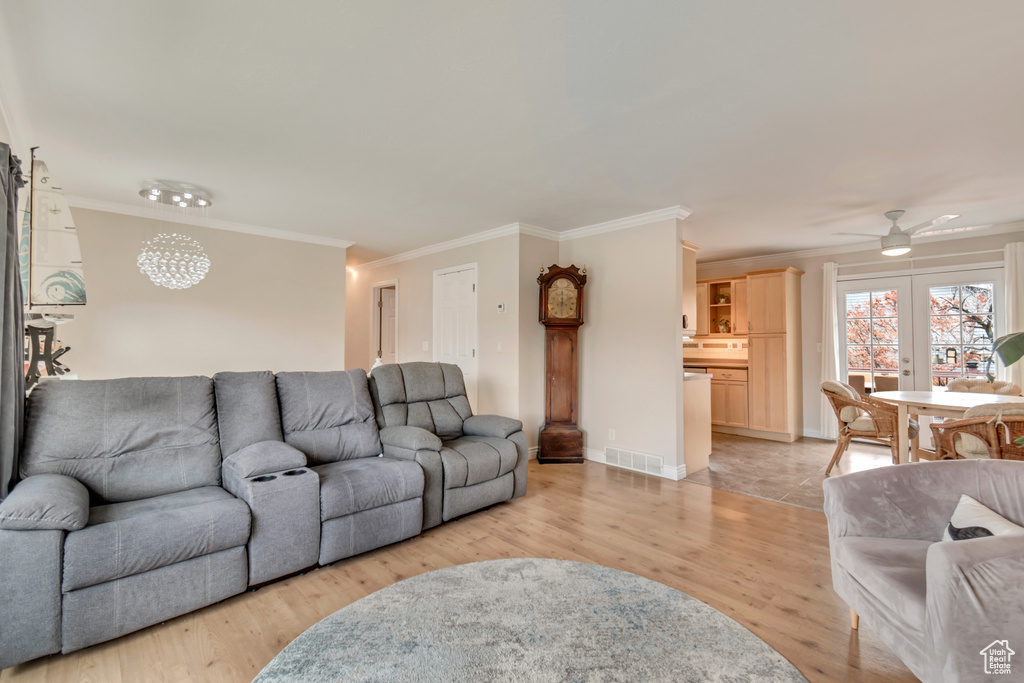 Living room featuring visible vents, crown molding, baseboards, light wood-style floors, and a ceiling fan