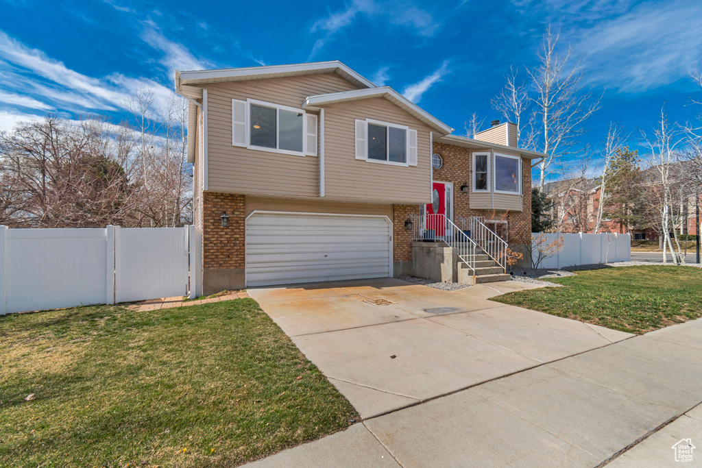 Split foyer home with brick siding, a front lawn, fence, driveway, and an attached garage