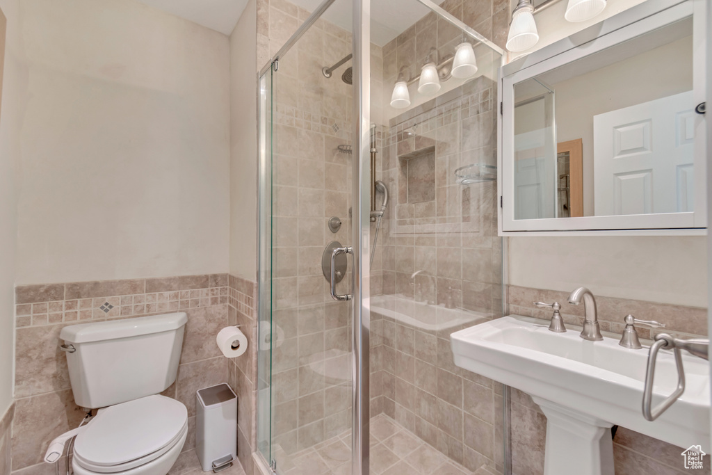 Full bathroom featuring a wainscoted wall, toilet, a stall shower, tile walls, and a sink