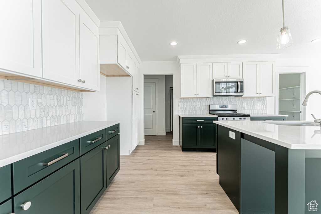 Kitchen featuring stainless steel appliances, green cabinets, white cabinets, light countertops, and decorative backsplash