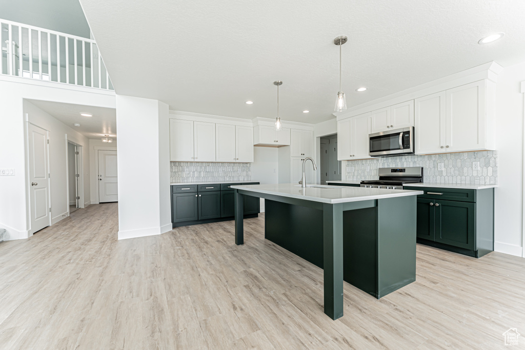 Kitchen featuring appliances with stainless steel finishes, light countertops, tasteful backsplash, white cabinetry, and light wood-type flooring