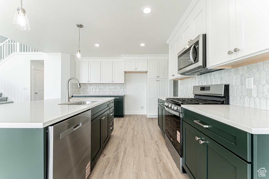 Kitchen with stainless steel appliances, green cabinetry, white cabinetry, light wood-style floors, and light countertops