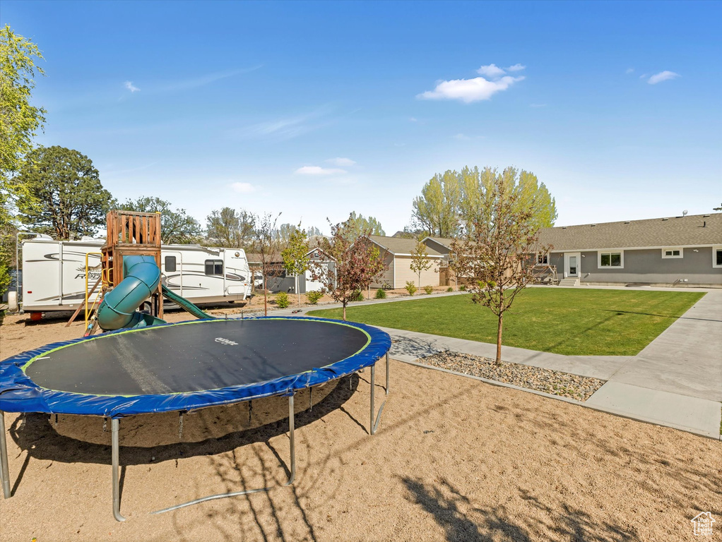 View of grassy yard with a trampoline, a playground, and a residential view