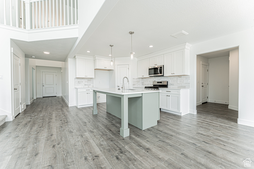 Kitchen featuring appliances with stainless steel finishes, decorative backsplash, light countertops, light wood-type flooring, and white cabinetry