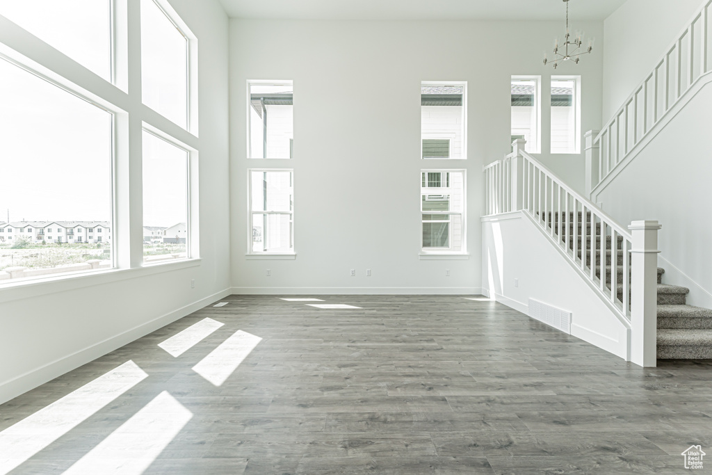 Unfurnished living room with stairway, a chandelier, wood finished floors, and a towering ceiling