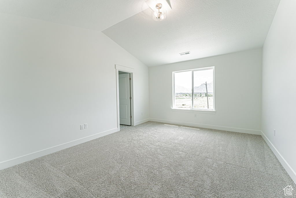 Spare room featuring light carpet and vaulted ceiling