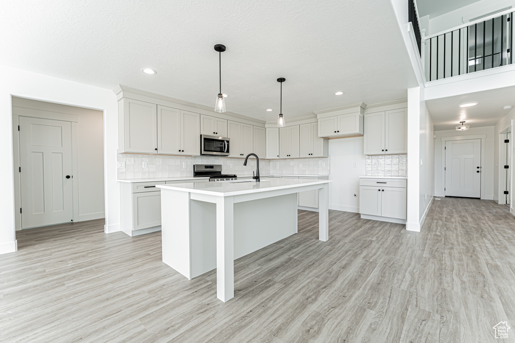 Kitchen with stainless steel appliances, light countertops, backsplash, light wood-style floors, and recessed lighting