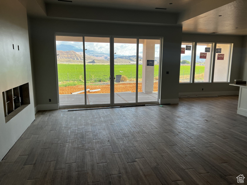Unfurnished living room featuring dark wood-style floors, a mountain view, baseboards, and plenty of natural light