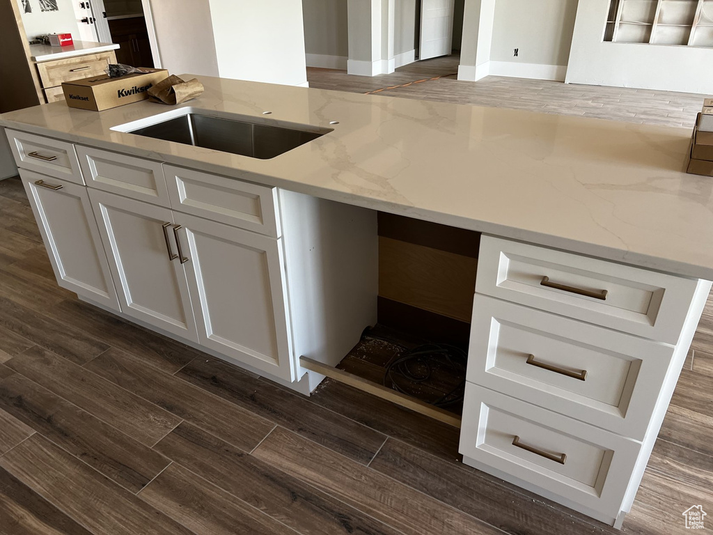 Kitchen featuring dark wood-type flooring, white cabinetry, light stone countertops, and a sink