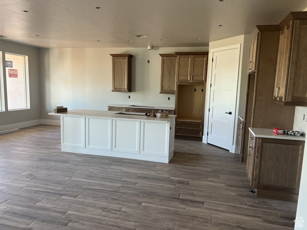 Kitchen with a center island, wood finished floors, baseboards, brown cabinetry, and recessed lighting