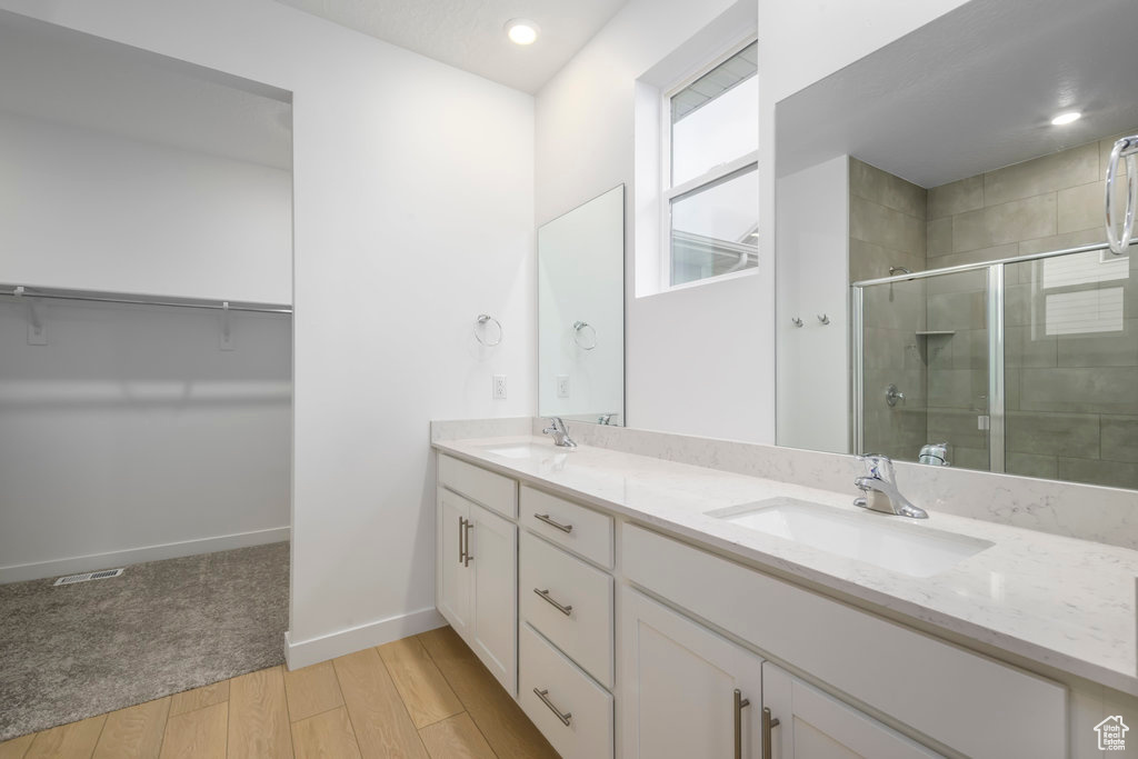 Full bath featuring baseboards, double vanity, a stall shower, wood finished floors, and a sink