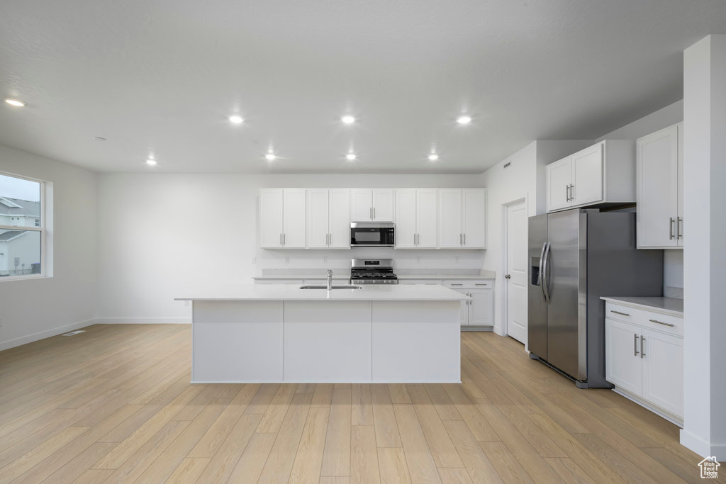 Kitchen with light wood-style flooring, appliances with stainless steel finishes, white cabinetry, and light countertops