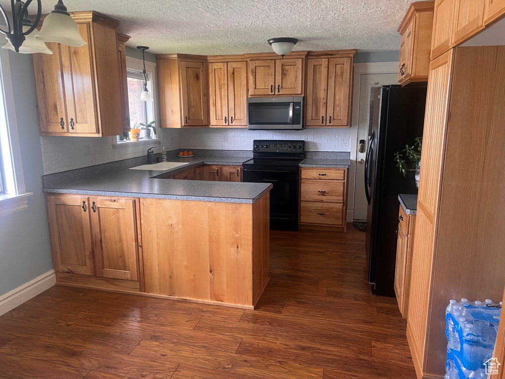 Kitchen with black appliances, dark wood-style flooring, a peninsula, backsplash, and a textured ceiling