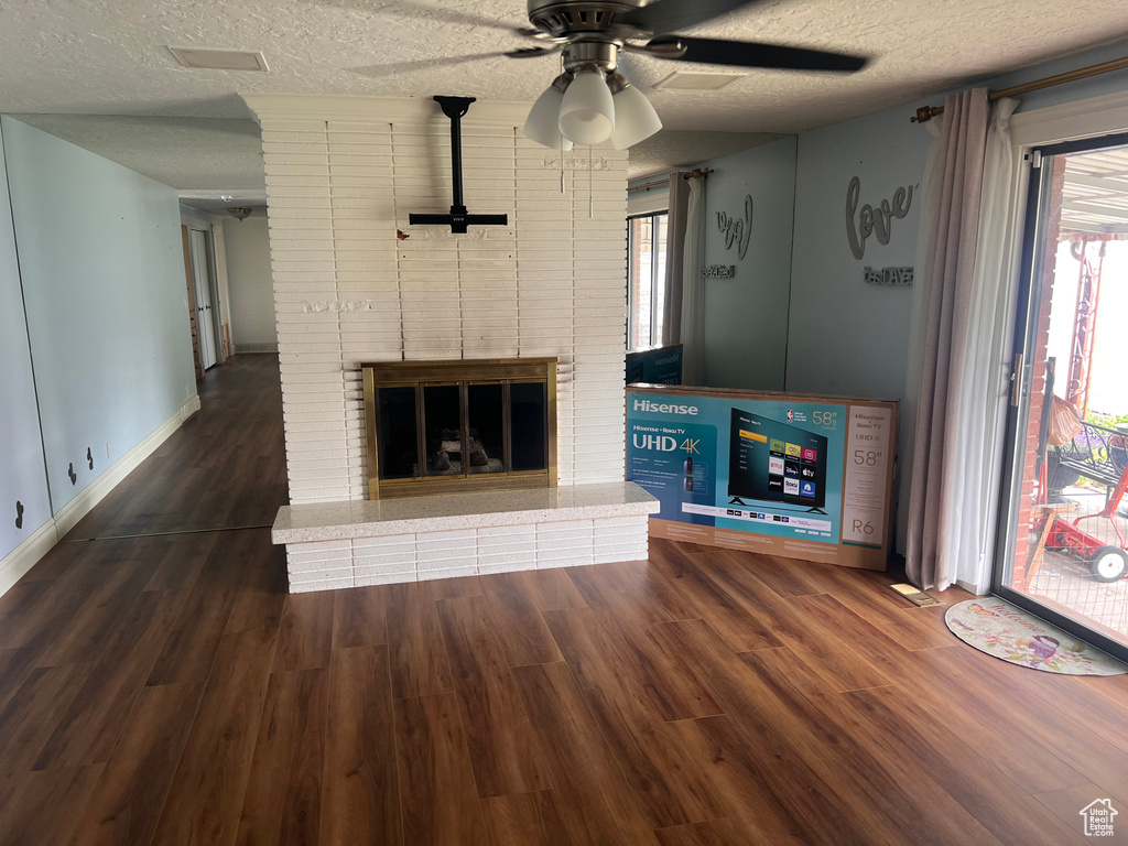 Unfurnished living room with a textured ceiling, wood finished floors, a ceiling fan, baseboards, and a fireplace
