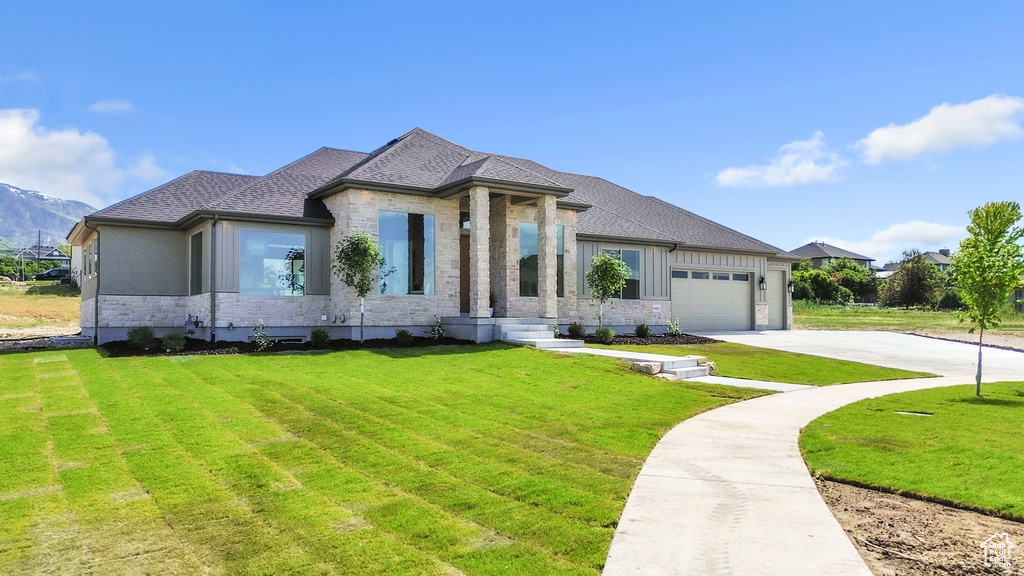 View of front of property featuring stone siding, a front yard, a garage, and driveway