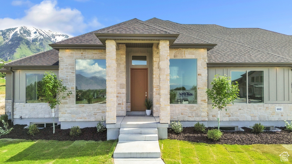 View of front facade with stone siding, a shingled roof, a mountain view, and a front yard