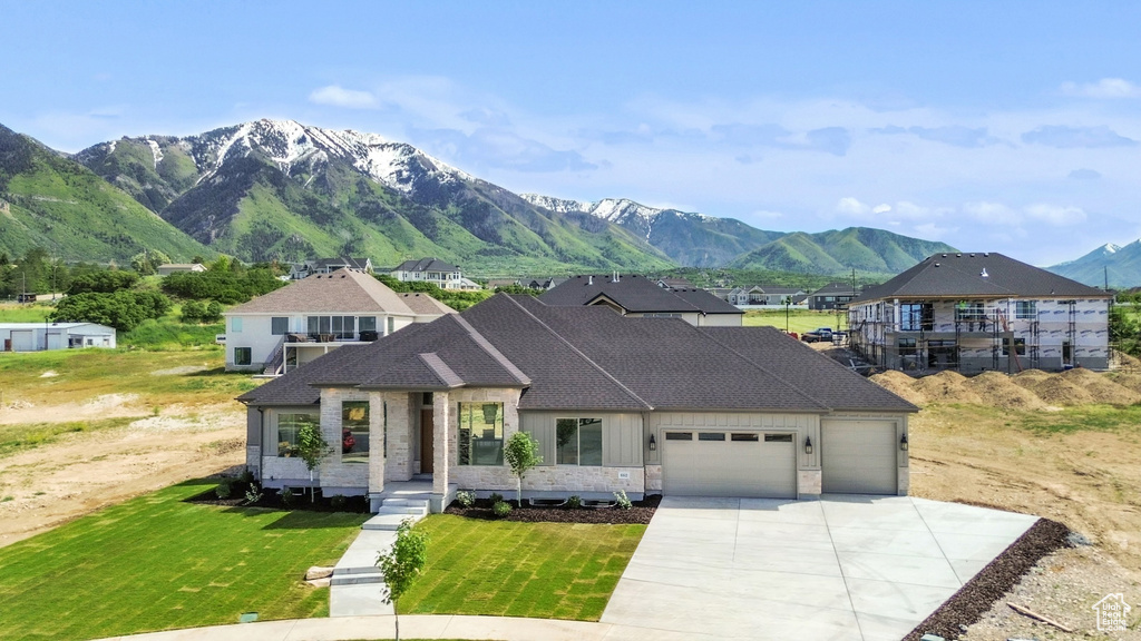 French country style house featuring a garage, a mountain view, driveway, a front lawn, and roof with shingles