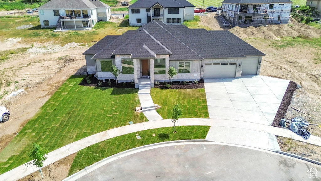 View of front facade featuring an attached garage, concrete driveway, roof with shingles, and a front yard