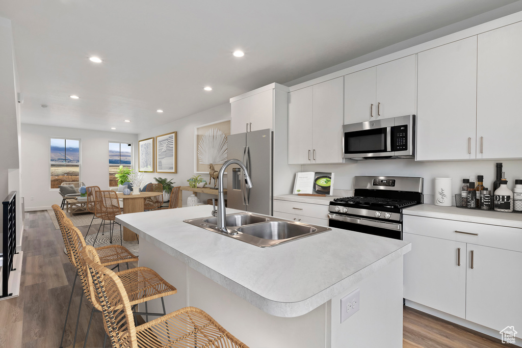 Kitchen with a kitchen bar, a sink, wood finished floors, recessed lighting, and stainless steel appliances