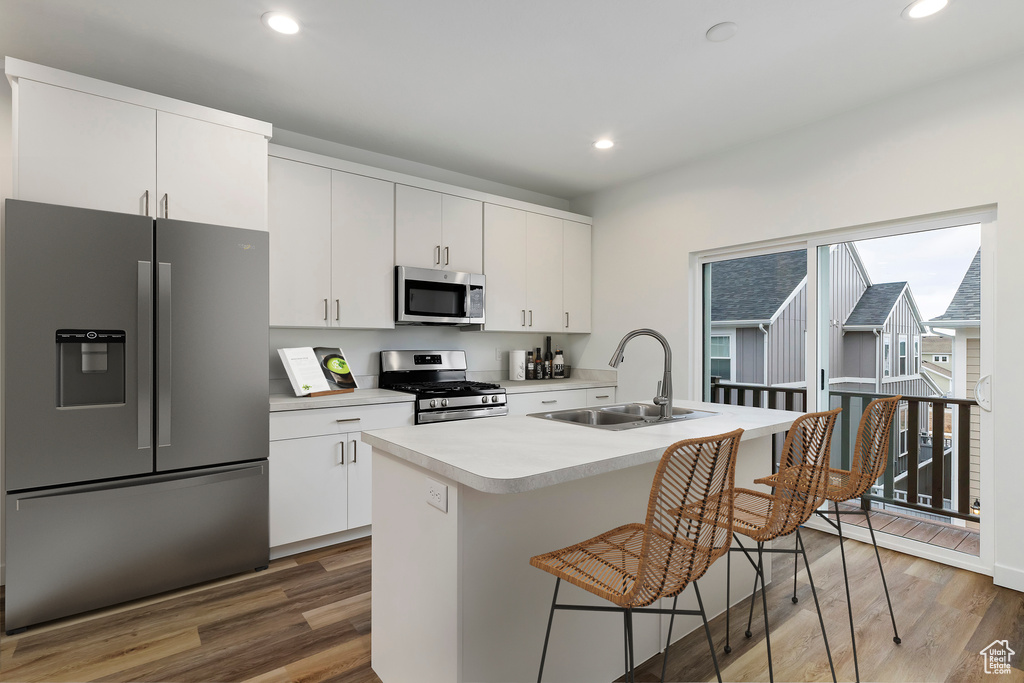 Kitchen featuring wood finished floors, a sink, stainless steel appliances, light countertops, and a kitchen breakfast bar