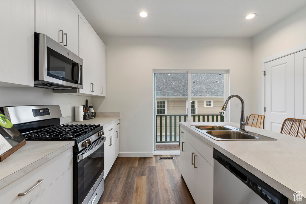 Kitchen with a sink, appliances with stainless steel finishes, dark wood-style flooring, and light countertops