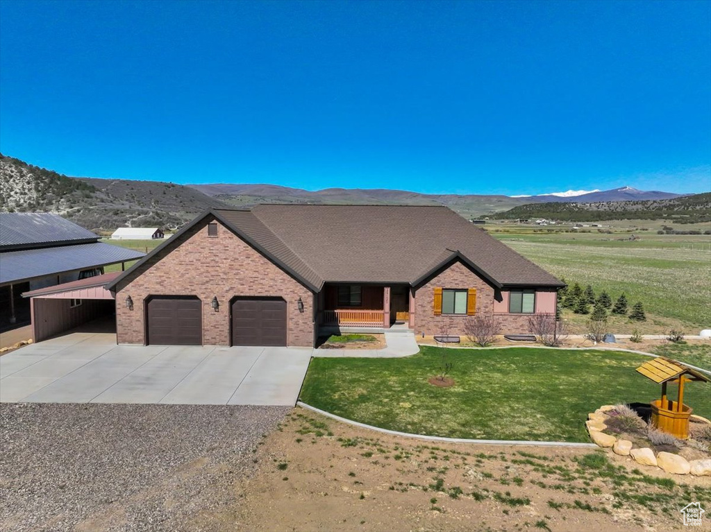 View of front of property featuring a mountain view, brick siding, concrete driveway, a garage, and a front yard