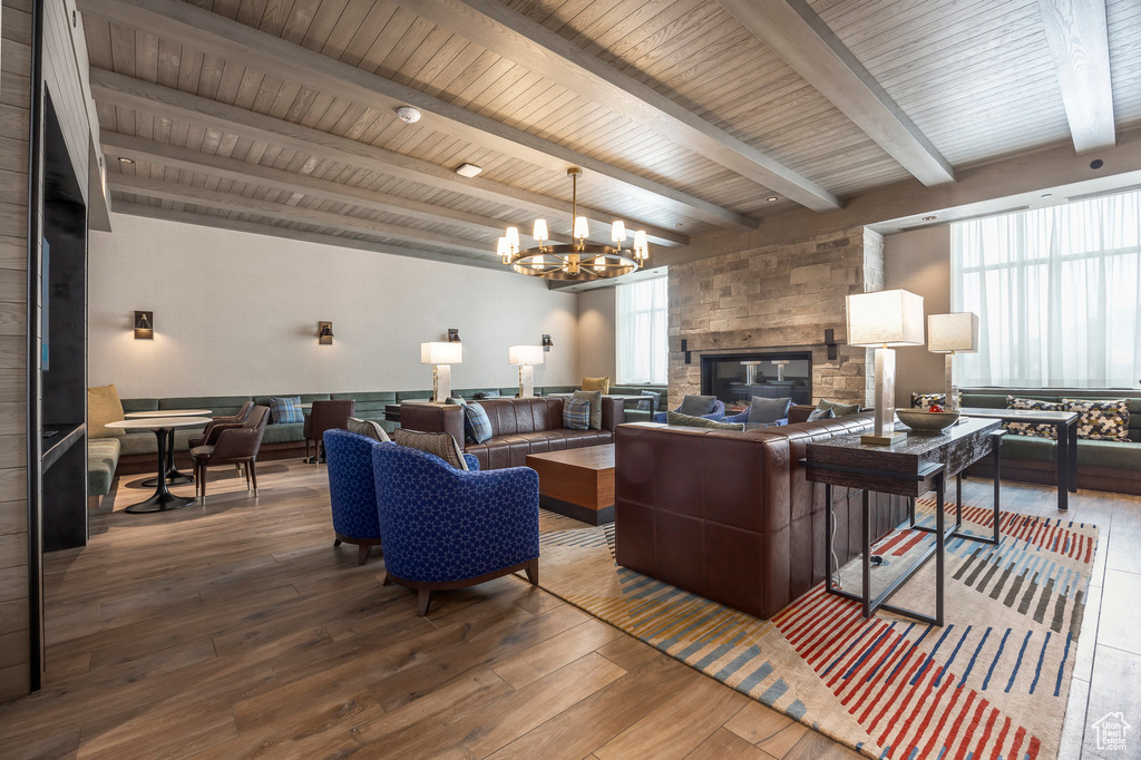 Living area featuring an inviting chandelier, beam ceiling, a stone fireplace, wood-type flooring, and wooden ceiling