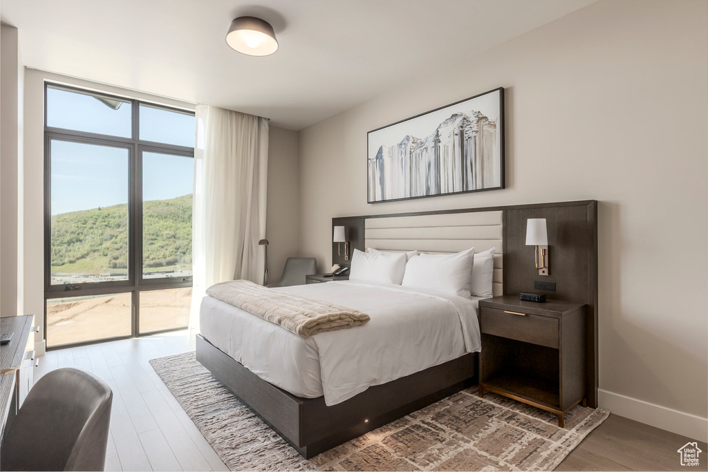 Bedroom with access to outside, wood finished floors, expansive windows, and baseboards