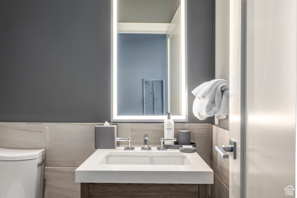Half bath featuring visible vents, tile walls, toilet, wainscoting, and vanity