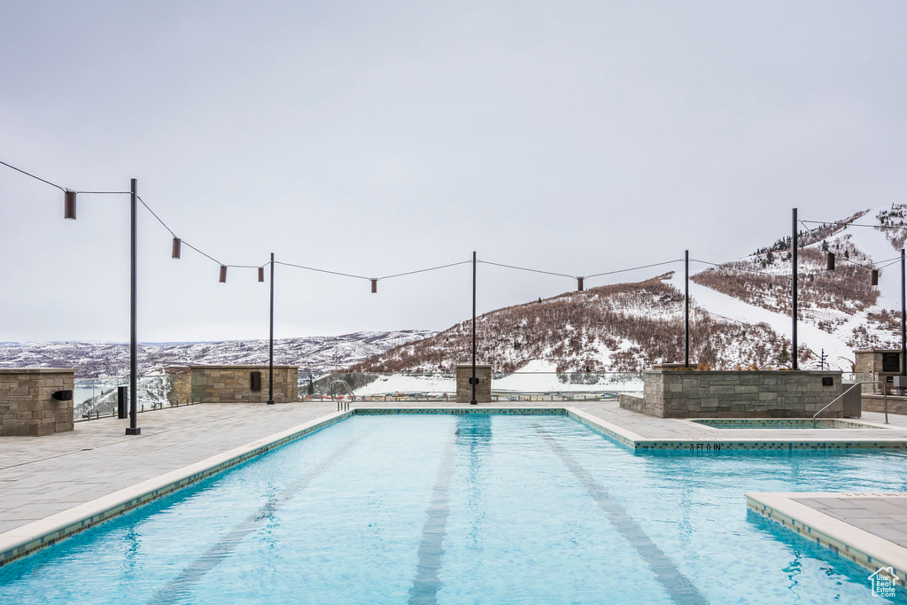 Snow covered pool featuring a patio area, an outdoor pool, and a mountain view