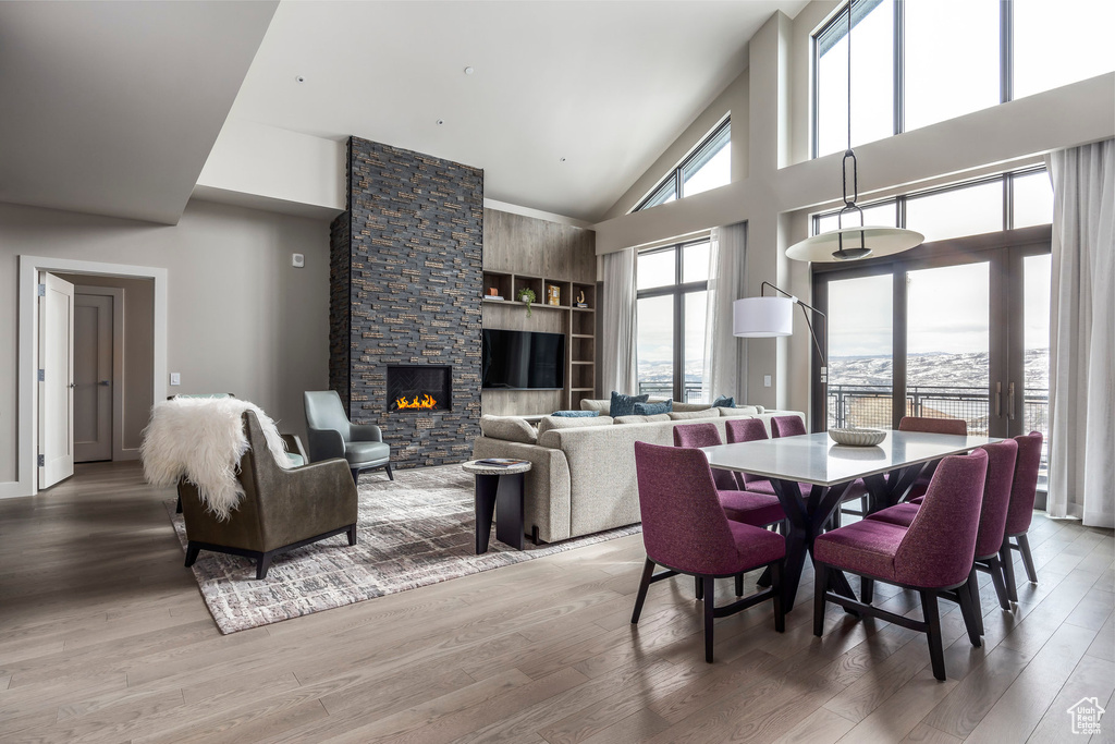 Dining area featuring a stone fireplace, light wood-type flooring, and a towering ceiling