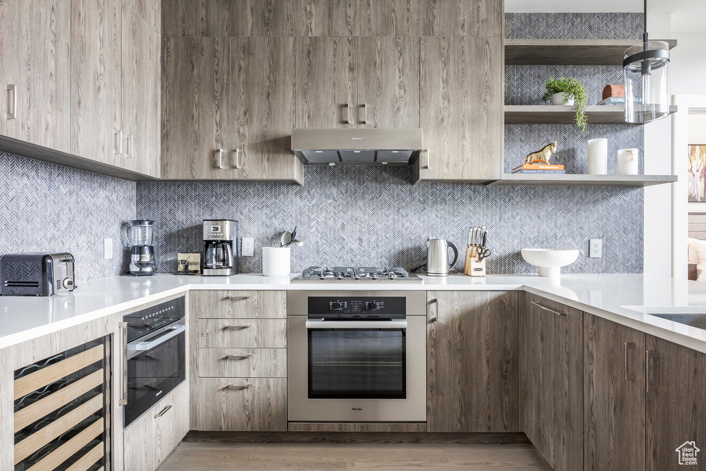 Kitchen featuring modern cabinets, stainless steel appliances, light countertops, decorative backsplash, and extractor fan