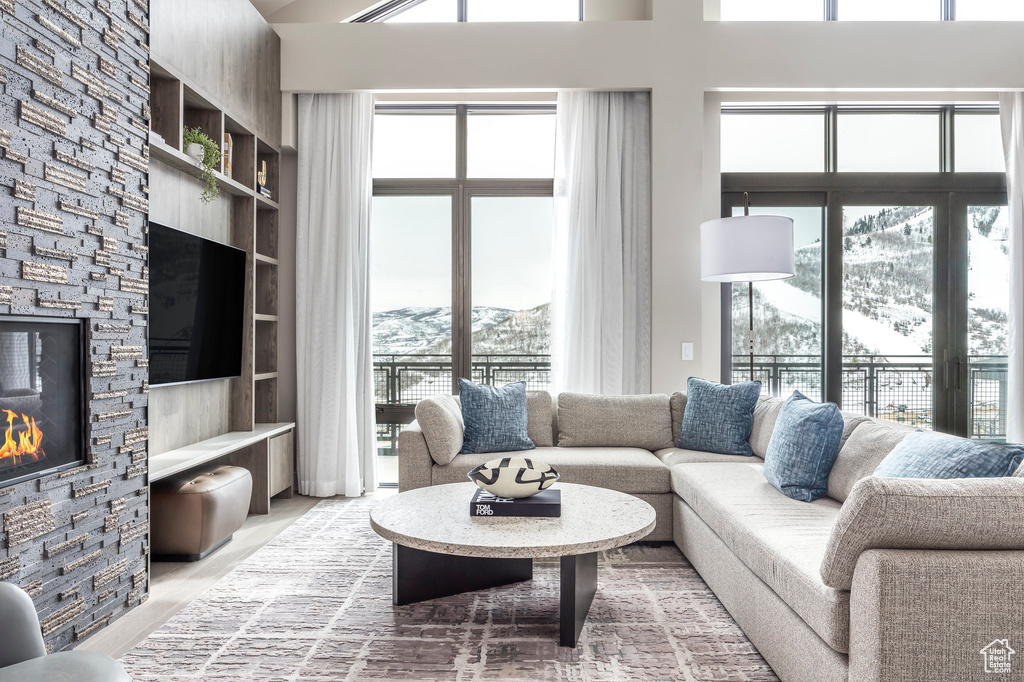 Living room with light wood-style floors, a stone fireplace, and a towering ceiling