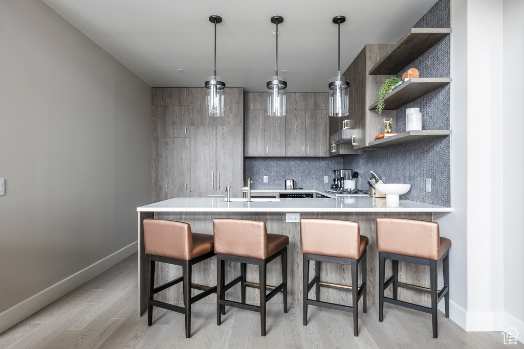 Kitchen featuring tasteful backsplash, light wood finished floors, light countertops, a peninsula, and open shelves
