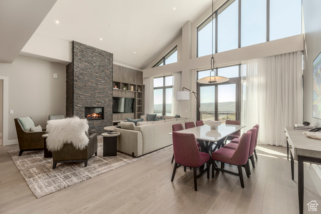 Dining space featuring light wood-style flooring, a stone fireplace, and a towering ceiling