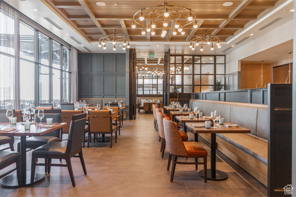 Dining area featuring a chandelier, a towering ceiling, wood ceiling with exposed beams, plenty of natural light, and coffered ceiling
