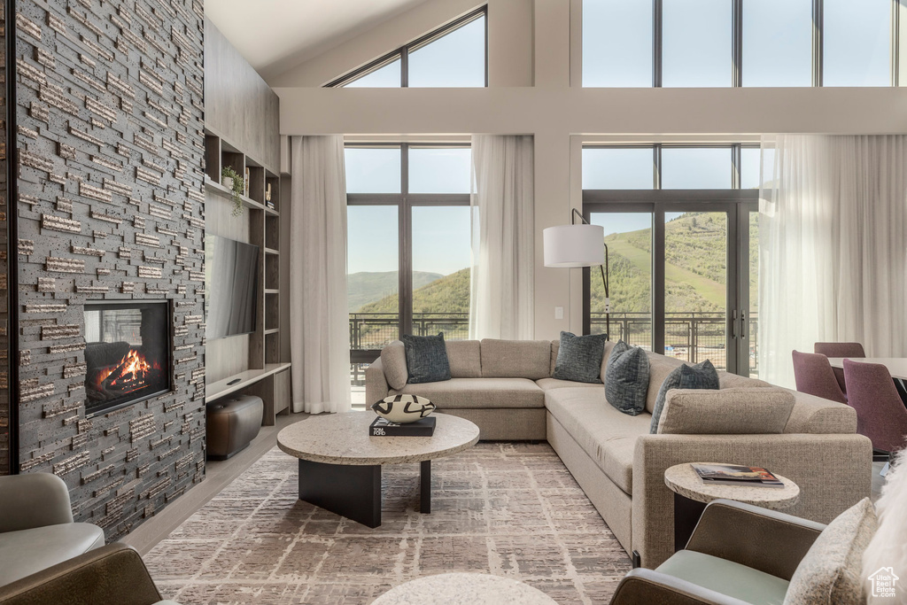 Living area with a mountain view, healthy amount of natural light, built in shelves, a stone fireplace, and high vaulted ceiling