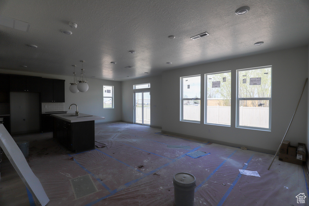 Unfurnished living room featuring a textured ceiling, a sink, and visible vents