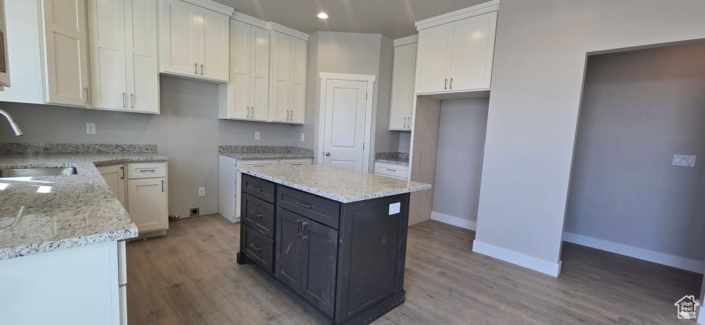 Kitchen with white cabinetry, light stone countertops, a sink, and wood finished floors