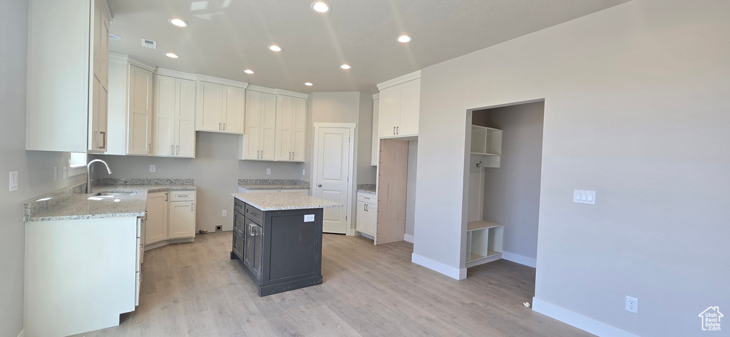 Kitchen with a sink, light stone counters, recessed lighting, light wood-style flooring, and baseboards