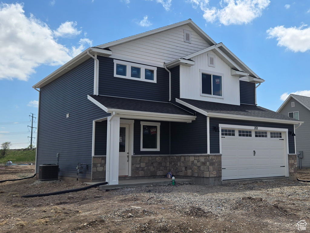Craftsman house with central AC unit, stone siding, an attached garage, and driveway